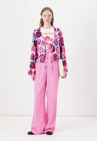 Colorful floral-patterned cardigan with shades of pink and blue, paired with loose pink pants and a light handbag. Black footwear included.