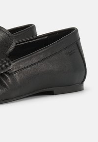 Μαύρα μοκασίνια από δέρμα με σούρες, χαμηλές επίπεδες φτέρνες και διακριτικές λεπτομέρειες στο ράψιμο.