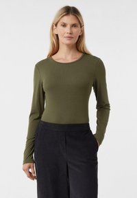 Bluzka z długim rękawem w oliwkowej zieleni, z prążkowan�ą fakturą i okrągłym dekoltem. Połączona z ciemnymi, szerokimi spodniami. Prosty, dopasowany fason.