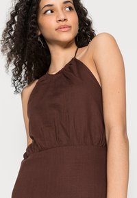 Vestido marron, sem mangas, com decote halter e cintura elástica, apresentando um tecido suave e texturizado.