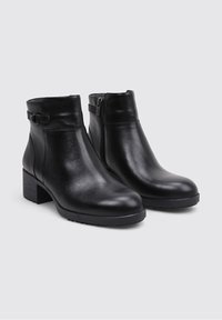 Par de botas de cuero negro hasta el tobillo con tacones bajos, cremalleras laterales y hebillas decorativas sobre un fondo gris claro.