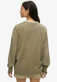 Sudadera verde oliva de manga larga, cuello redondo y puños acanalados. Presenta un corte relajado y una tela suave y texturizada. Sin logotipos visibles.