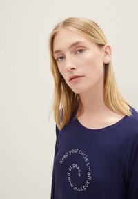 Camisa de manga larga azul marino con cuello redondo que presenta un texto en espiral blanco que dice: "Mantén tu círculo pequeño y tu mente en paz."