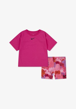 T-shirt rose à manches courtes avec logo noir, associé à un short rose à motif floral comprenant différentes nuances de rouge et de violet.