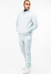 Lichtblauwe geruite trainingsoutfit gemaakt van zachte stof; heeft witte strepen, geribbelde manchetten en een logopatch op de borst en broek.