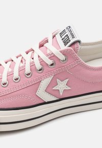 Rosa kanvas sneakers med vita snörningar, gummisula och svarta detaljer. Har en vit stjärnlogotyp och "All Star"-etikett på tungan.