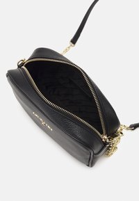 Bolsa cruzada de cuero negro con cierre de cremallera, herrajes en tono dorado y forro interior texturizado que presenta un patrón sutil.