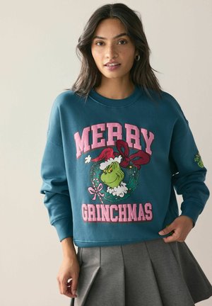 Tannengrüner Sweatshirt mit "MERRY GRINCHMAS" in pinkem Text, verziert mit einer Grinch-Grafik inmitten eines Kranzes und festlichen Akzenten.