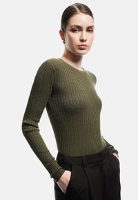 Top a maniche lunghe a coste di colore verde oliva, con scollatura a girocollo e design aderente. Abbinato a pantaloni neri su misura.