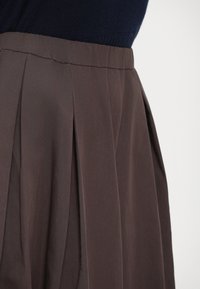 Hooggesneden bruine geplooide rok gecombineerd met een donkerblauwe gebreide top, afgebeeld vanaf de taille naar beneden tegen een witte achtergrond.