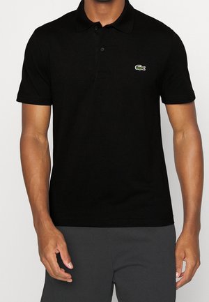 Polo noir à manches courtes, avec un col côtelé, une patte de boutonnage à trois boutons et un petit logo crocodile vert sur la poitrine.