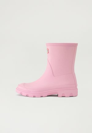 Rosa gummistøvel med en glatt overflate, rund tå og teksturert såle. Har en logopatch på ytre ankel. Hult form, midt på leggen høyde.