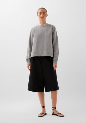 Grauer Sweatshirt mit lockerer Passform, Rundhalsausschnitt und geripptem Saum, kombiniert mit fließenden schwarzen Culottes und schwarzen Sandalen mit Riemchen.