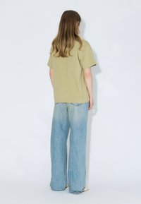 T-shirt en coton vert olive avec épaules tombantes et coupe décontractée, associé à un jean large bleu clair taille haute.