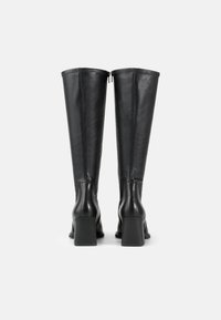 Bottes en cuir noir montantes avec un talon carré, texture lisse et fermeture éclair à l'arrière. Design simple et construction sans couture.