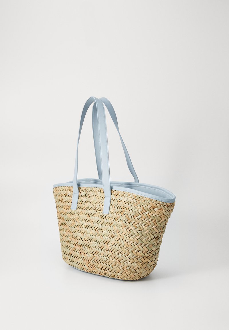 Sac fourre-tout en paille tissée avec des poignées et des bordures en cuir synthétique bleu clair, présentant un motif naturel et un design sans fermeture.