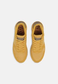 Gule sportssko med mesh- og ruskinds-overdel, rund tå, kontrasterende grå accenter og teksturerede indlægssåler.