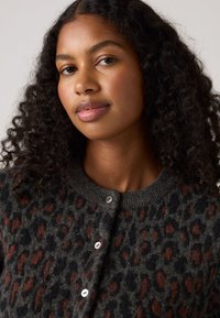 Kardigan s leopardím vzorom v tmavo šedej farbe, s hnedými akcentmi, okrúhlym výstrihom a gombíkovým zapínaním. Mäkkučký materiál a voľný strih.