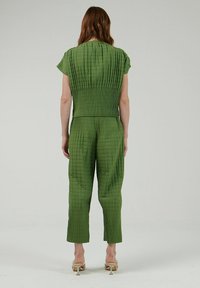 Mono acolchado verde con mangas cortas, cuerpo ajustado y pantalones acampanados, con pliegues horizontales y verticales para dar textura.