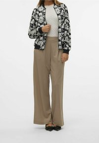 Czarna bomberka w kwiaty z prążkowanymi mankietami, teksturowana kremowa bluzka i szerokie beżowe spodnie, połączone z czarnymi szpilkami.