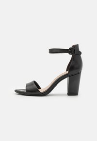 Black leather high-heeled sandal with a wide toe strap, ankle strap featuring a buckle, and a geometric block heel for stability.