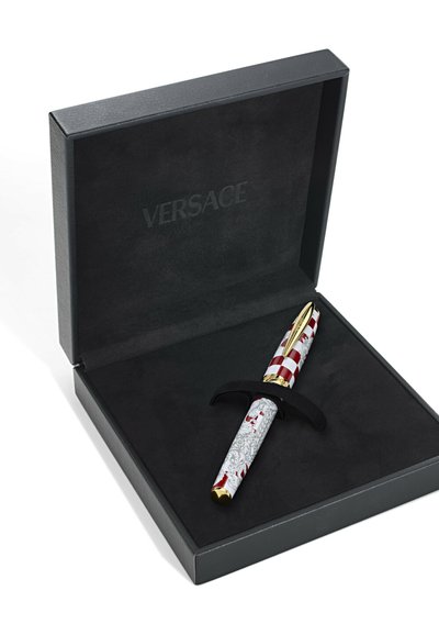 Versace toll egy fekete dobozban, piros és fehér mintás hengerrel, arany díszítésekkel és texturált markolattal, fekete állványon.