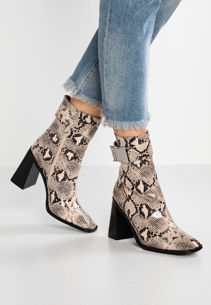 Stivaletti con tacco a caviglia in pelle effetto serpente beige e nera, con chiusura a zip e accentuazione in metallo. Tacco a blocco in gomma.