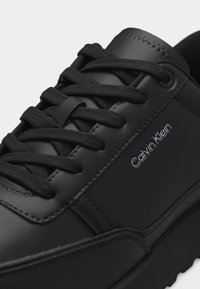 Μαύρο δερμάτινο αθλητικό παπούτσι με μαύρα κορδόνια και λογότυπο Calvin Klein στο πλάι, με λεπτομερή ραφές και υφασμένο πέλμα.