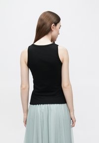 Fekete ujjatlan felső sima, rugalmas anyagból. Testhezálló fazon, kerek nyakkivágással, hátulnézetből, világoszöld szoknyával párosítva.