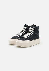 Wysokie trampki wykonane z czarnego zamszu z białymi sznurówkami, z grubą kremową podeszwą i kontrastującymi białymi przeszyciami.