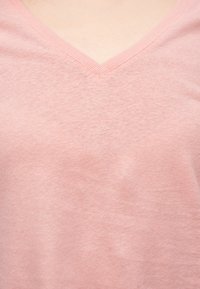 Απαλό ροζ μπλουζάκι με λαιμόκοψη σε σχήμα V που δείχνει το λαιμό και την άνω περιοχή του στήθους ενός ατόμου, με ορατή υφή υφάσματος.