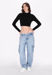 Fekete bordázott, hosszú ujjú crop top, amely laza, világoskék cargo farmernadrággal van párosítva, oldalsó zsebekkel és egyenes szabással.