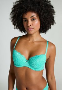 Turquoise kant-bh met bloemenpatronen, onderlegsteun, verstelbare banden en een kleine decoratieve strik in het midden.