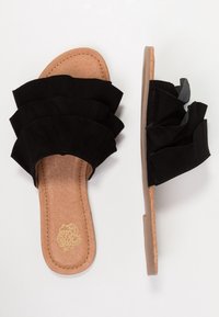 Svarta mocka flip-flops med lager av volanger, beige innersulor och en platt gummisula. Har en slät yta och öppen tå.