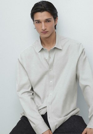 Light gray button-up shirt made of textured fabric, featuring a collar, long sleeves, and subtle seam detailing, paired with dark pants.