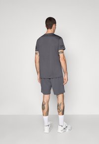 Grå trenings t-skjorte med korte ermer og ingen synlige logoer, sammen med matchende shorts. Hvite joggesko og ankelsokker i hvitt.