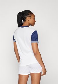 Witte sport T-shirt met blauwe korte mouwen en gestreepte accenten, gecombineerd met witte shorts, met een gladde stoftextuur en een getailleerd ontwerp.