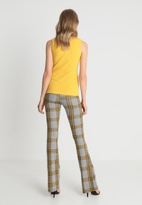 Žlutý žebrovaný tílko v kombinaci s šedými a žlutými kostkovanými zvonovými kalhotami. Oblečení má přiléhavý střih s texturovaným povrchem.