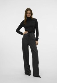 Maglione nero a collo alto abbinato a pantaloni larghi grigio scuro, con vita elastica e texture liscia, su sfondo bianco.