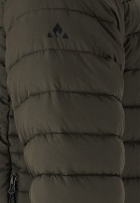 Manteau matelassé vert olive avec des manches bouffantes, présentant une couture matelassée, une logo noir sur le haut du bras et une fermeture éclair noire à l'ourlet.