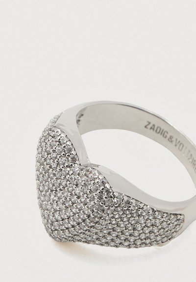 Zilveren ring in hartvorm met kleine heldere edelstenen die het vooroppervlak bedekken en met de gegraveerde merknaam aan de binnenkant van de band.