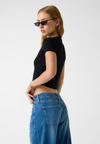Czarna bluzka z krótkim rękawem w połączeniu z jasnoniebieskimi, wysokim stanem, dopasowanymi jeansami o casualowej teksturze denimu z tylnymi kieszeniami.