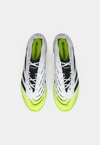 Scarpe sportive bianche con strisce nere, superficie testurizzata e una suola gialla brillante con un design ondulato, etichettate "PREDATOR" all'interno.
