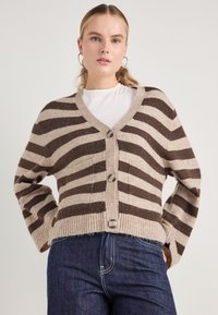 Ριγέ καζάκα σε μπεζ και καφέ με V λαιμόκοψη, ribbed στρίφωμα και κλείσιμο με τέσσερα κουμπιά; διαθέτει κατεβασμένους ώμους και υφή υφάσματος.