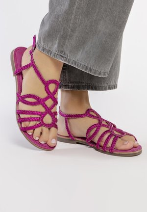 Sandalias trenzadas de color rosa con suelas planas, que presentan correas entrelazadas y los dedos de los pies al descubierto. El material parece suave con un acabado liso.