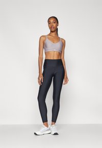 Sports bra in light gray, high-waisted black leggings, and white athletic shoes. The outfit features a sleek, form-fitting design and smooth texture.