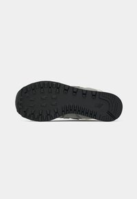 Suola di una sneaker con scanalature profonde in gomma nera, caratterizzata da un logo vicino al tallone su uno sfondo grigio chiaro.