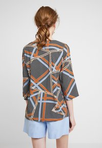 Kortærmet skjorte med et geometrisk mønster i sort, orange og blå. Lavet af et glat stof med et let design.