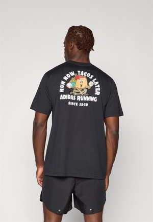 T-shirt in cotone nera con una grafica colorata di un taco e il testo "CORRI ORA, TACOS DOPO" sul retro, maniche corte e vestibilità ampia.