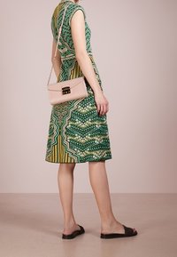 Zelené šaty s potiskem, krátkými rukávy, přiléhavým pasem a rozšířenou sukní. V kombinaci s růžovou kabelkou přes rameno a černými sandály na klínku.